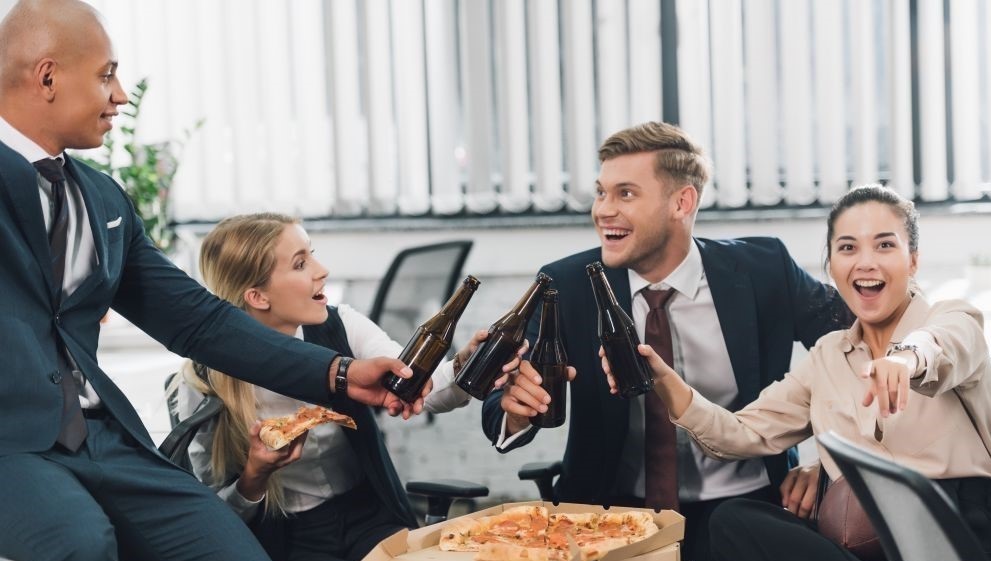 Kollegen im Büro stoßen an und essen Pizza