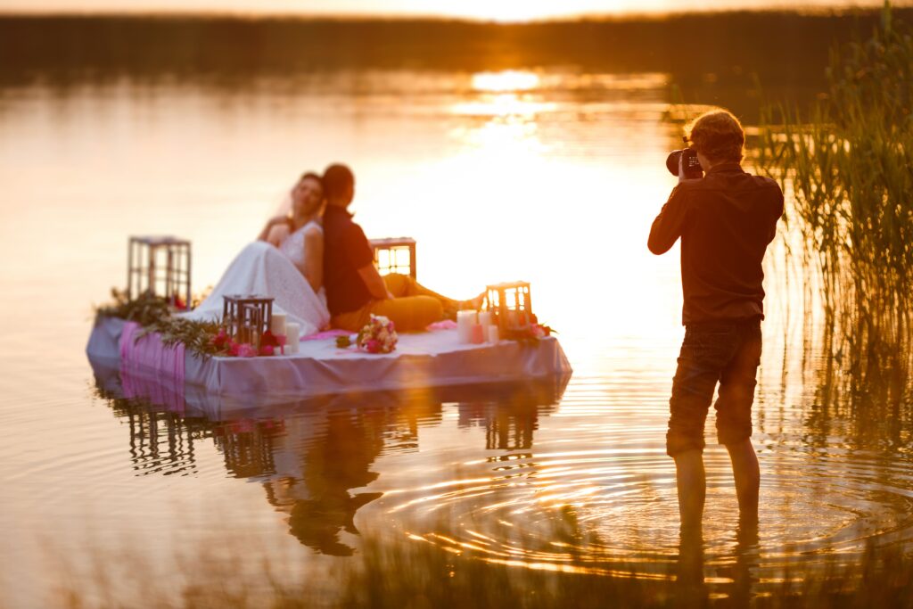 Bild eines Hochzeitsfotografen im See, der ein Brautpaar auf einem Floß fotografiert.