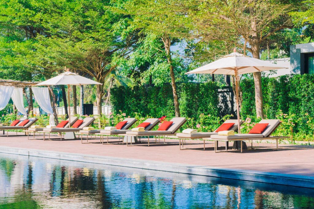 Bild vom Pool eines luxuriösen Urlaubresorts mit mehreren Liegen und Sonnenstühlen mit Sonnenschirmen.