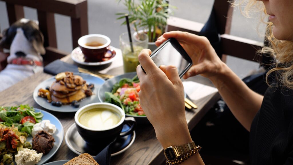 Bild einer jungen Frau, die ein Foto von ihrem Essen macht.